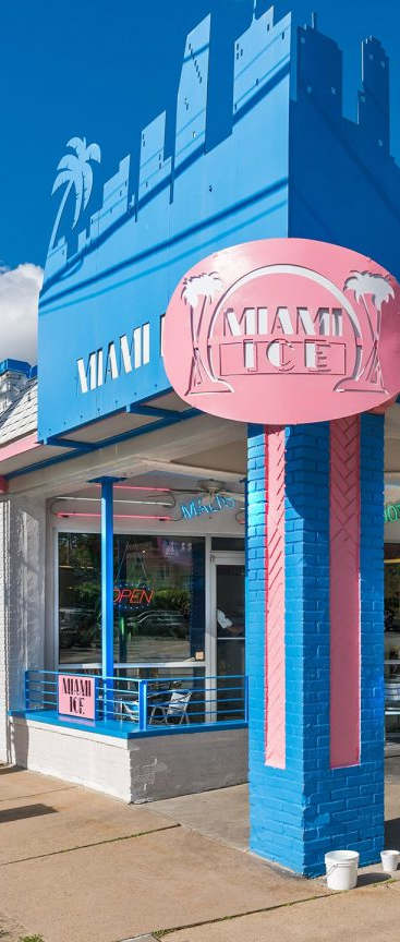 A woman in a red dress stands outside a building with a sign that reads "Miami Ice.".
