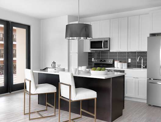A modern kitchen with a large island and two chairs. at The Elle on Lockwood Apartments, Webster Groves, MO, 63119