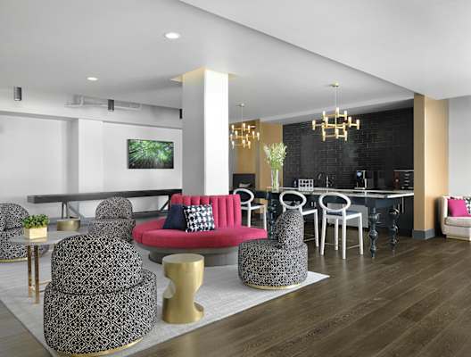 A modern living room with a red couch and grey ottoman. at The Elle on Lockwood Apartments, Webster Groves, MO, 63119