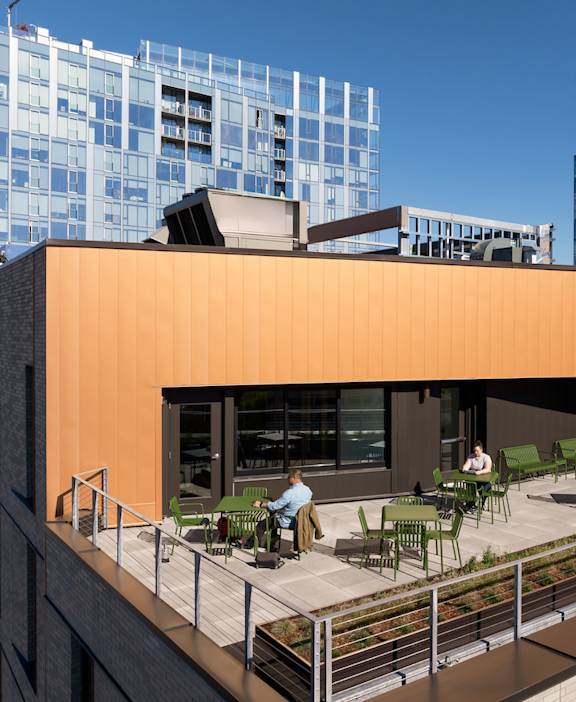 A modern building with a terrace and people sitting on chairs.
