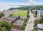 Thumbnail 7 of 11 - A large building complex with a green lawn in front and a city skyline in the background at Queen St East in Scarborough, ON