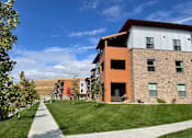 Thumbnail 4 of 27 - A modern building with a mix of stone and wood paneling is surrounded by a well-kept lawn and a clear blue sky.