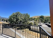 Thumbnail 20 of 27 - A balcony with a black railing overlooks a residential area with houses and trees.
