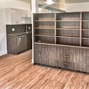 A kitchen with a wooden floor and a large wooden cabinet with drawers.