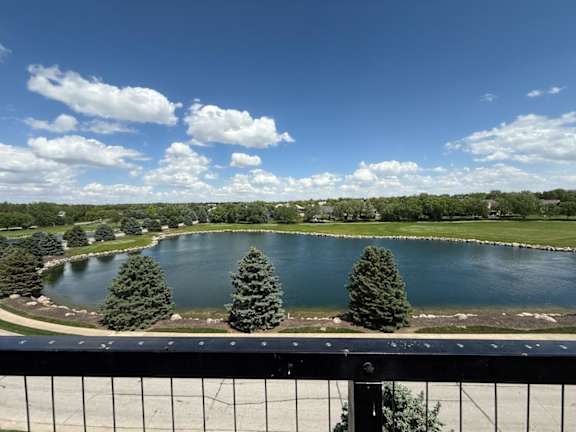 A pond surrounded by trees under a blue sky with clouds.
