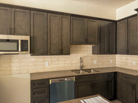a kitchen with deep brown cabinets, gray counters, and beige backsplash
