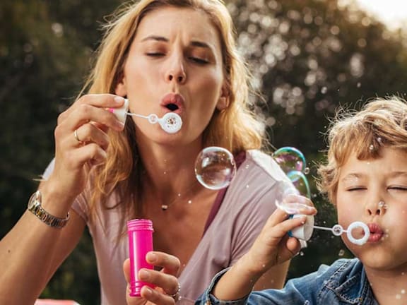 a woman and child blowing bubbles while sitting on the ground