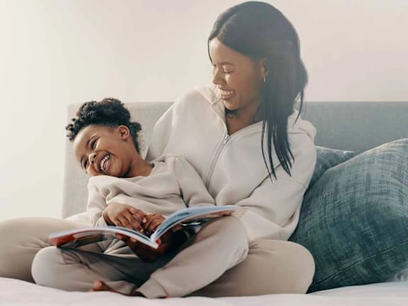 a woman and child reading a book on a couch