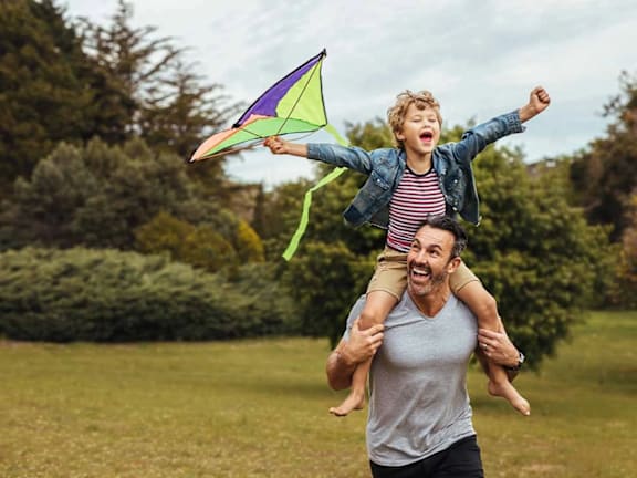 a man holding a child on his shoulders while flying a kite