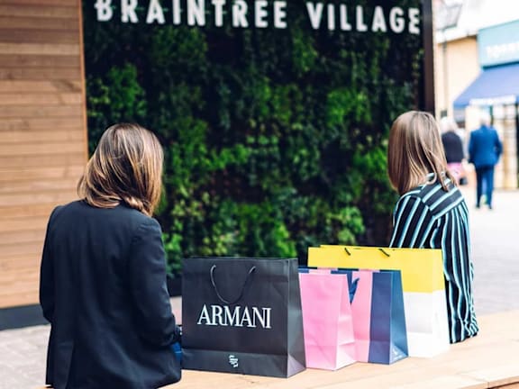 two women sitting with shopping bags in front of a store
