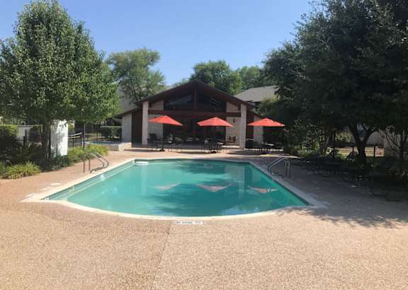 A swimming pool surrounded by trees and umbrellas.