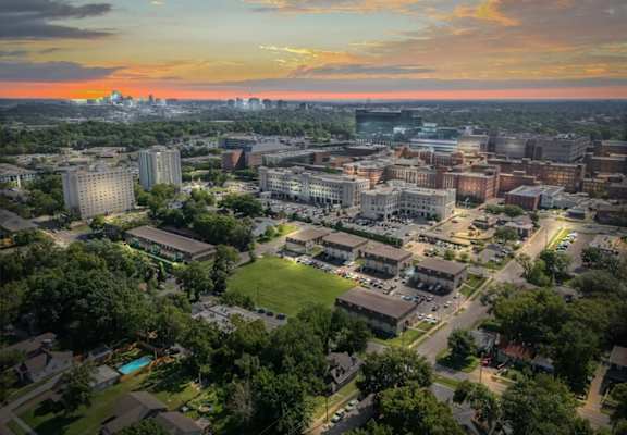A cityscape with buildings and greenery under a sunset sky.