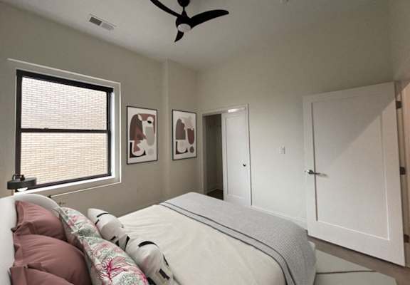 A bedroom with a bed, a window with blinds, a ceiling fan, and two framed pictures on the wall. at The Annex Apartments, Buffalo, NY, 14222