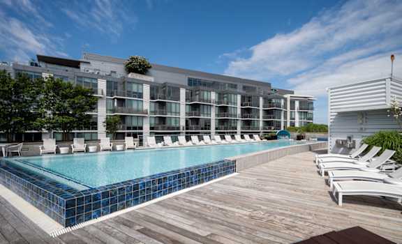 A large swimming pool with a wooden deck and lounge chairs in front of a modern building. at Dock 79, District of Columbia