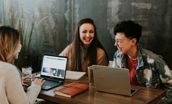three people sitting at a table with laptops
