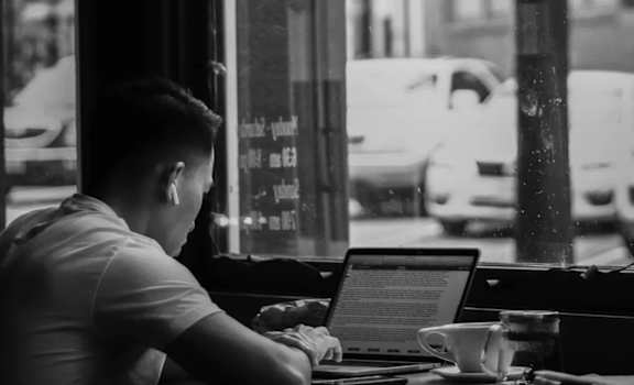 a man sitting in a window working on his laptop