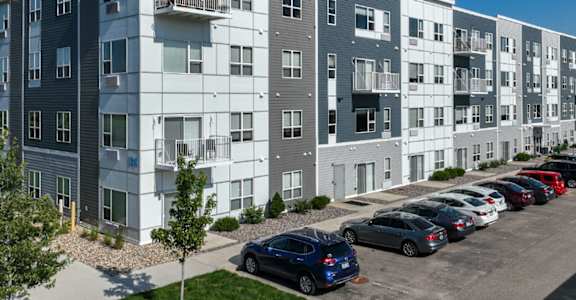 A row of modern apartment buildings with cars parked in front.