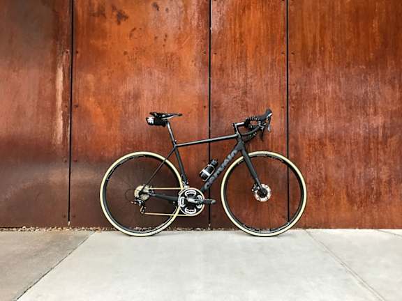 A black bicycle is leaning against a brown wall.