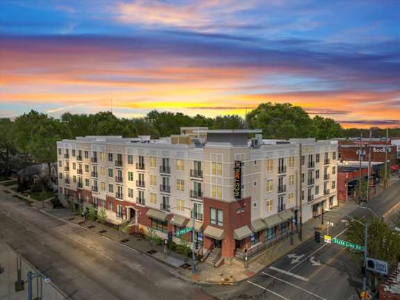 A sunset view of a street with a multi-story building on the corner.