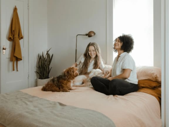 two women sitting on a bed with a dog