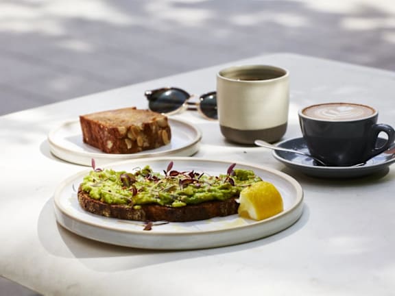 a plate of avocado toast and two cups of coffee on a table