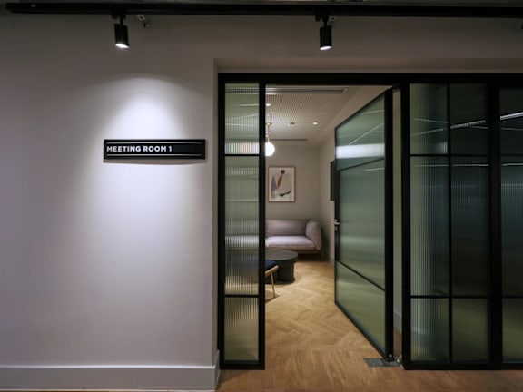 a corridor with glass doors and a white wall with a meeting room sign