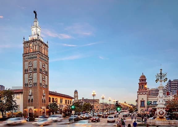 A city street with a large clock tower and a statue on a pole.
