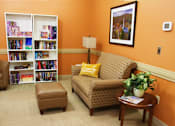 Thumbnail 3 of 8 - A living room with a couch, chair, ottoman, and bookshelves.