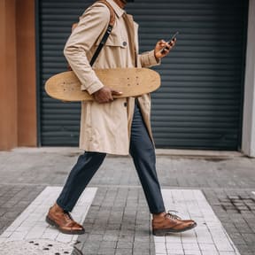 a man walking down the street holding a skateboard and looking at his phone