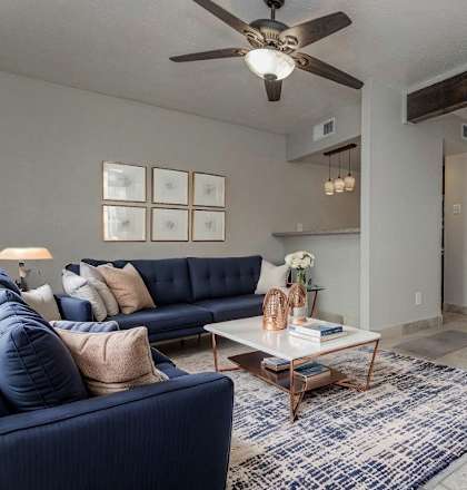 A living room with a blue sofa, a coffee table, and a ceiling fan.