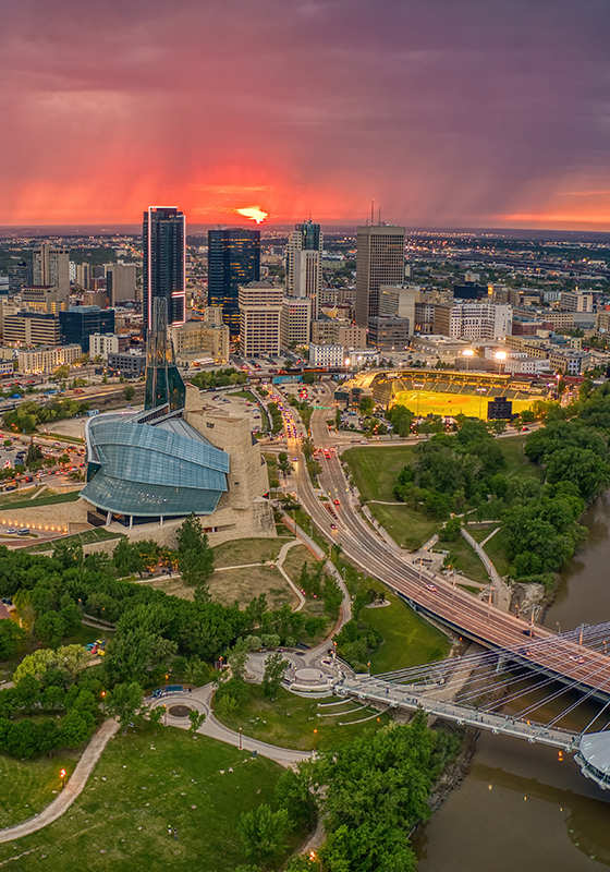 A cityscape with a sunset in the background and a bridge crossing a river.