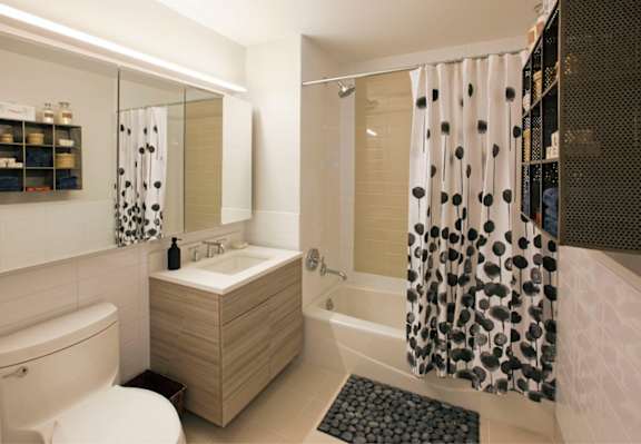 A bathroom with a white toilet, sink, and shower curtain at The Maximilian Apartments, New York, 11101