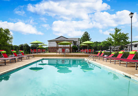 A pool with red chairs and a building in the background.