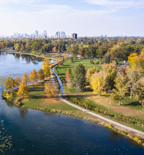 A serene park with a river, trees, and a city skyline in the distance.