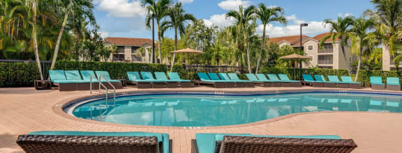 a resort style swimming pool with blue chaise lounge chairs and palm trees in the background