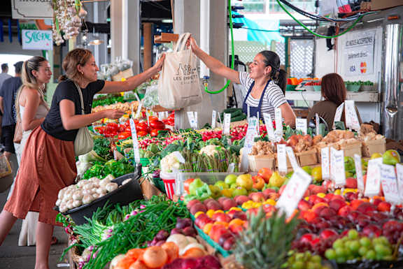 A woman is handing a bag to another woman at a fruit stand.