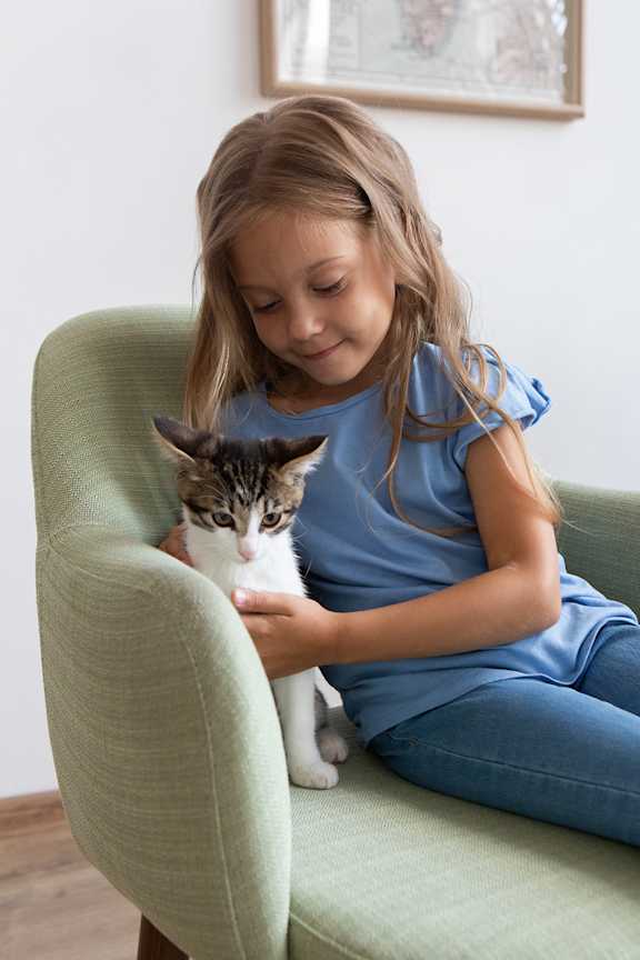 A young girl is sitting on a green chair holding a cat.