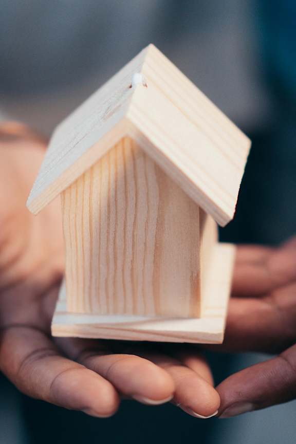 A small wooden house model is being held in a person's hand.