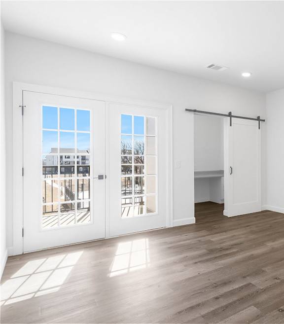 A room with white walls and wooden flooring, with a view of a building outside through the windows.