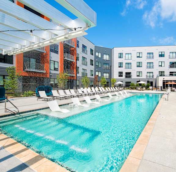 A large swimming pool with lounge chairs and a building in the background.