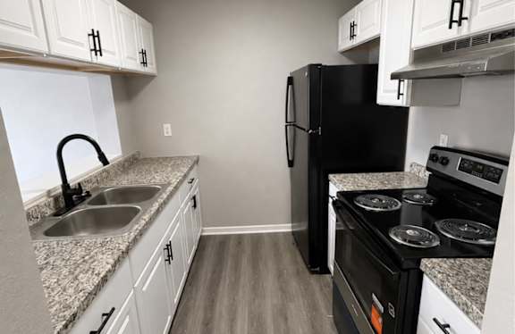 A black refrigerator sits in a kitchen with white cabinets and a granite countertop.