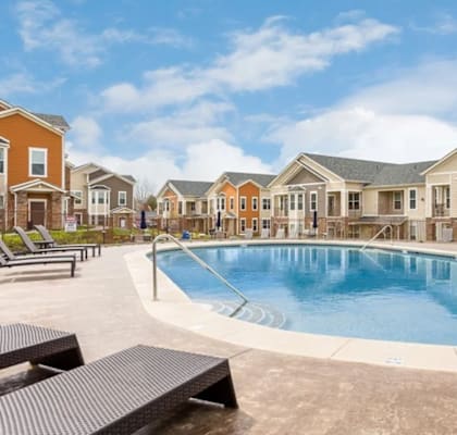A swimming pool surrounded by sun loungers and apartment buildings.
