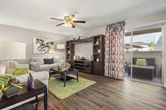 A living room with a grey couch, a coffee table, a ceiling fan, and a painting of a horse.