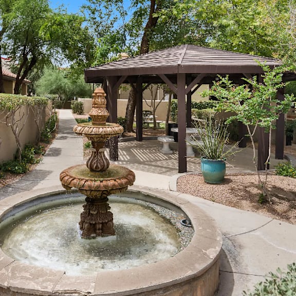 A fountain in the middle of a courtyard with a gazebo in the background.
