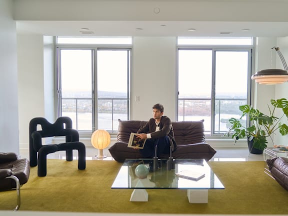 A man is sitting on a brown couch in a living room. at The Dale Apartments , Ottawa, ON