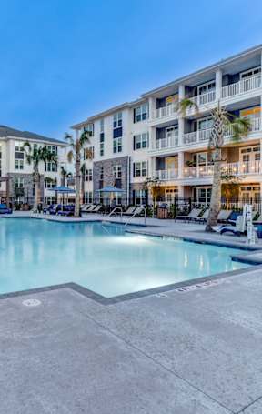 A large swimming pool is surrounded by a concrete patio and lounge chairs.
