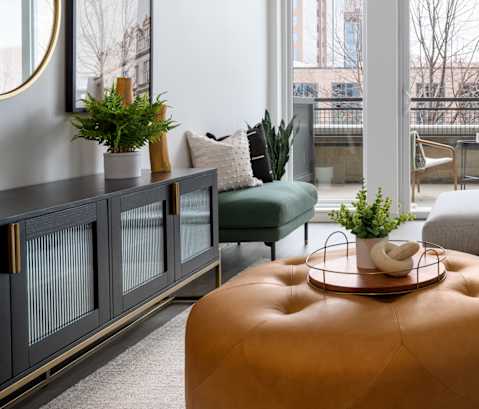 A living room with a grey couch, a brown ottoman, and a green chair.