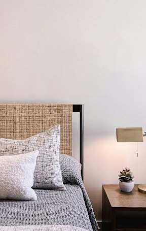 A bed with pillows and a small table with a plant and a lamp.