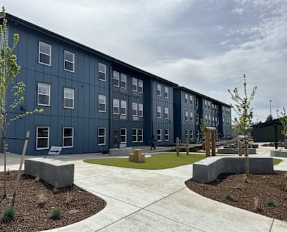 A modern building with a blue exterior and a courtyard with concrete benches and trees.