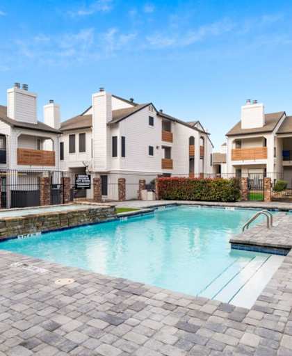 A swimming pool surrounded by a brick patio and apartment buildings.